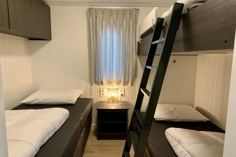 Camera da letto accogliente in chalet con due letti singoli, letto a castello, comodino e finestra.