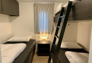Camera da letto accogliente in chalet con due letti singoli, letto a castello, comodino e finestra.