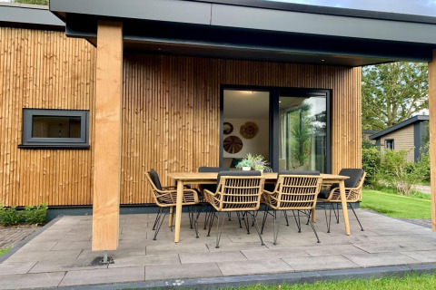 Modern chalet met een overdekte veranda, tuintafel en stoelen, in een groene omgeving in Nederland.
