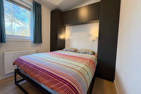 Soveværelse med dobbeltseng og farverigt betræk i Chalet nær Sint Maartenszee-stranden, Holland.