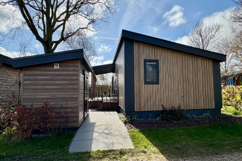 Modernes, holzverkleidetes Chalet nahe dem Sint Maartenszee Strand in den Niederlanden an einem sonnigen Tag.