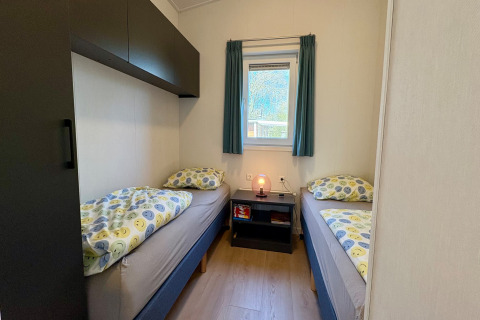 Deux lits simples avec une literie colorée, une table de nuit et une fenêtre dans une chambre près de la plage Sint Maartenszee.