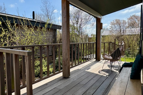 Holzveranda mit Stuhl und Bank im Chalet nahe Sint Maartenszee Beach, Niederlande, im Frühling.