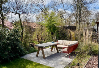 Zona patio con divano e tavolo in giardino verde presso Chalet vicino alla spiaggia Sint Maartenszee, Olanda.
