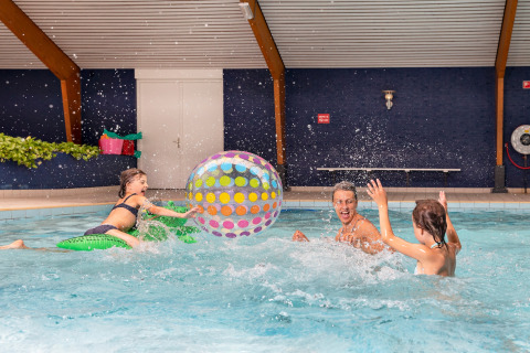 Gezin speelt met een kleurrijke strandbal in het binnenzwembad van chalet bij Sint Maartenszee Beach, Nederland.