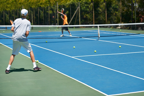 Twee mensen spelen tennis op een buitenplein bij Chalet nabij Sint Maartenszee Beach met ballen op de baan.