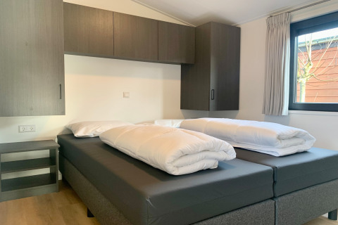 Moderne soveværelse i Chalet i Sint Maartenszee, Holland, med to senge, dyner og skabe ved vinduet.