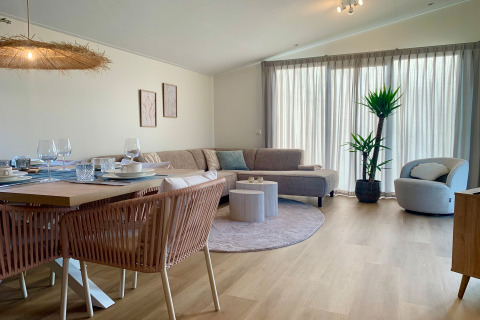 Helles Wohnzimmer im Strandhaus-Chalet in Sint Maartenszee mit Couch, Essbereich und Topfpflanze.