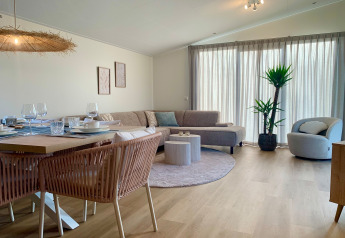 Helles Wohnzimmer im Strandhaus-Chalet in Sint Maartenszee mit Couch, Essbereich und Topfpflanze.