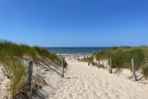 Zandweg tussen grasduinen naar het Sint Maartenszee strand met blauwe lucht en zee in Nederland.