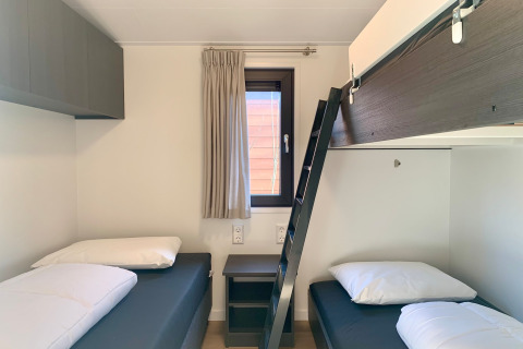 Camera moderna in chalet vicino alla spiaggia con tre letti singoli, scala a soppalco e finestra.