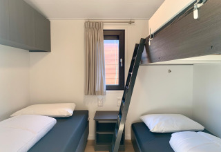 Moderne slaapkamer met drie enkele bedden, ladder naar bovenbed en raam in chalet bij zee.