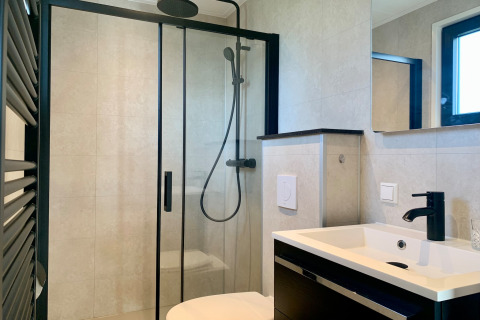 Baño moderno con cabina de ducha negra y grifería negra en chalet de Sint Maartenszee cerca de la playa.