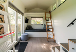 Licht, modern tiny house interieur in Nederland met slaapzolder, ladder en grote ramen naar buiten.