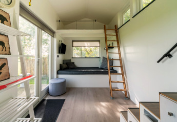 Licht, modern tiny house interieur in Nederland met slaapzolder, ladder en grote ramen naar buiten.