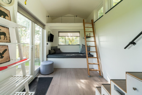 Interior de tiny house moderna y luminosa en Países Bajos, con altillo, escalera y amplias ventanas.