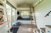 Intérieur lumineux d’une tiny house moderne aux Pays-Bas avec mezzanine, échelle, et grandes fenêtres.