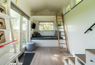 Interior de tiny house moderna y luminosa en Países Bajos, con altillo, escalera y amplias ventanas.