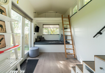 Intérieur lumineux d’une tiny house moderne aux Pays-Bas avec mezzanine, échelle, et grandes fenêtres.