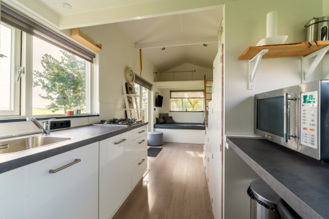 Lichte, moderne tiny house keuken in Nederland met witte kasten, raam en comfortabele zithoek.