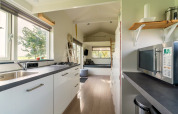 Lichte, moderne tiny house keuken in Nederland met witte kasten, raam en comfortabele zithoek.