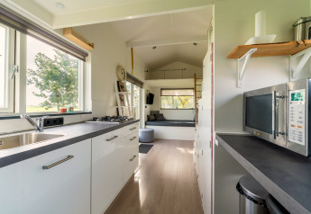 Lichte, moderne tiny house keuken in Nederland met witte kasten, raam en comfortabele zithoek.