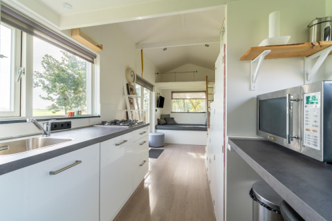 Cocina moderna en tiny house en Holanda con gabinetes blancos, ventana grande y acogedora sala de estar.