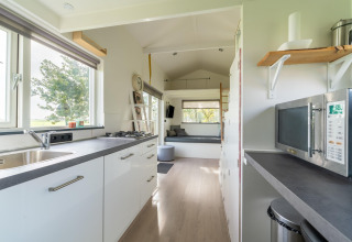 Cocina moderna en tiny house en Holanda con gabinetes blancos, ventana grande y acogedora sala de estar.