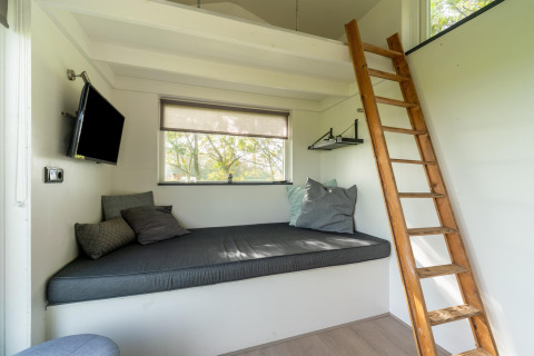 Interior acogedor de una tiny house en los Países Bajos con sofá, cama en altillo y escalera de madera.
