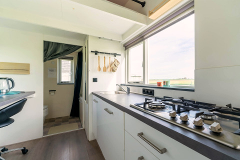 Lichte, moderne keuken in een tiny house in Nederland met gaskookplaat, spoelbak en groot raam met uitzicht.