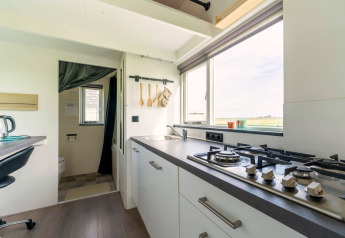 Lichte, moderne keuken in een tiny house in Nederland met gaskookplaat, spoelbak en groot raam met uitzicht.