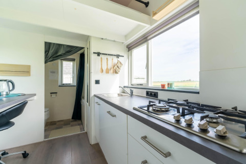 Cocina luminosa y moderna de una tiny house en Países Bajos con estufa de gas, fregadero y ventana amplia.