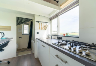 Cocina luminosa y moderna de una tiny house en Países Bajos con estufa de gas, fregadero y ventana amplia.