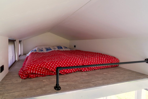 Slaaploft met laag plafond en rood met witte stippen dekbed in een tiny house in Nederland.