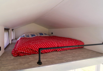 Slaaploft met laag plafond en rood met witte stippen dekbed in een tiny house in Nederland.