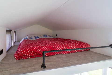 Altillo de techo bajo con edredón rojo de lunares en una tiny house en los Países Bajos.