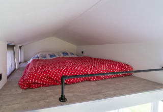 Altillo de techo bajo con edredón rojo de lunares en una tiny house en los Países Bajos.