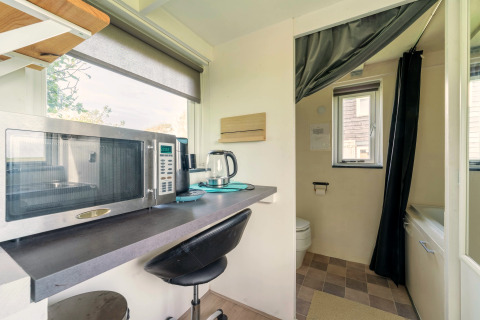 Compacte keukenhoek met microgolfoven en waterkoker in tiny house in Nederland, zicht op de badkamer.