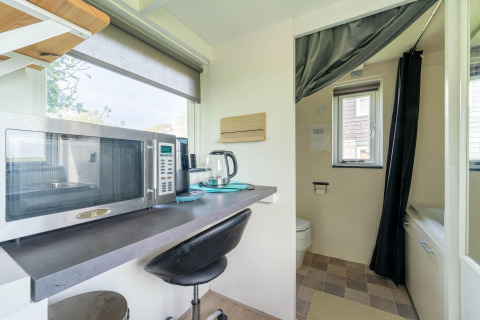 Pequeña cocina con microondas y hervidor en una tiny house en Países Bajos, vista al baño al fondo.