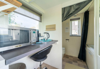 Pequeña cocina con microondas y hervidor en una tiny house en Países Bajos, vista al baño al fondo.