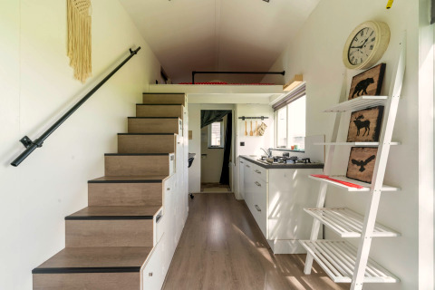 Interieur van een tiny house in Nederland met een trap, keuken en decoratieve rekken aan de muur.