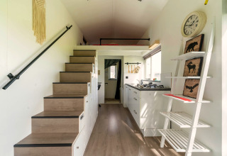 Interieur van een tiny house in Nederland met een trap, keuken en decoratieve rekken aan de muur.