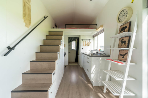 Interior de una tiny house moderna en los Países Bajos con escalera, cocina y estantería decorativa.