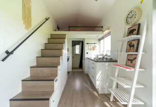 Interior de una tiny house moderna en los Países Bajos con escalera, cocina y estantería decorativa.