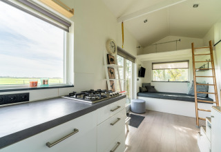 Interior moderno y luminoso de una tiny house en los Países Bajos con cocina, sofá y altillo.