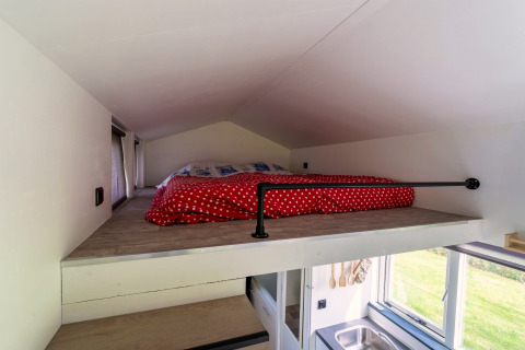 Slaapgedeelte op de mezzanine met rood dekbed in een tiny house in Nederland, vanuit trap gezien.