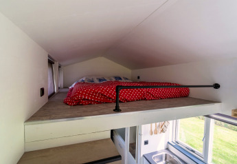 Slaapgedeelte op de mezzanine met rood dekbed in een tiny house in Nederland, vanuit trap gezien.