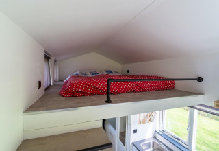 Dormitorio tipo altillo con techo bajo y edredón rojo en una tiny house de los Países Bajos.