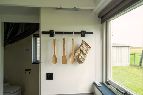 Keukengerei en ovenwant hangen aan de muur in een Tiny House in Nederland, zicht op het raam.