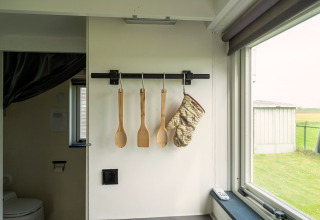 Keukengerei en ovenwant hangen aan de muur in een Tiny House in Nederland, zicht op het raam.